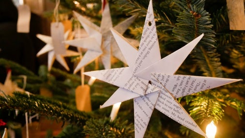 A close up of a paper star in a Christmas tree lit up by a bulb.